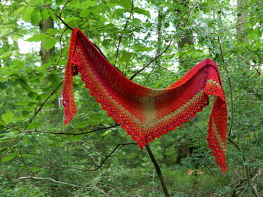 Gehäkeltes dreieckiges Tuch in Rot-Orange-Grün mit Spitze, aufgehängt an Ästen im Wald