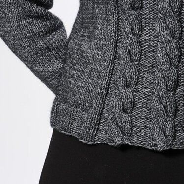 Close-up of women's grey melange sweater showing cable patterns and a ribbed hem.