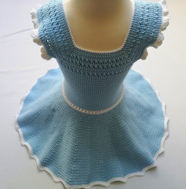 Hellblaues gehäkeltes Kinderkleid auf Mannequin mit quadratischem Ausschnitt, kurzen Rüschenärmeln und weißer Borte