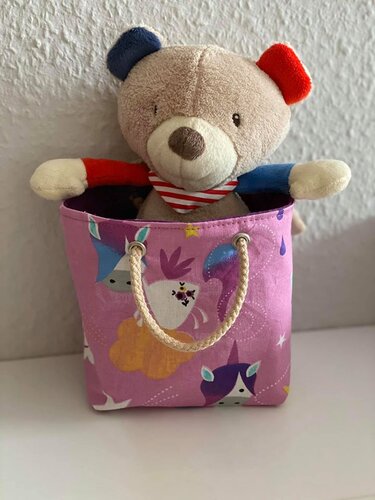 Kleine rosa-lila Stofftasche mit Einhornmuster und Kordelgriffen, mit Teddybär darin