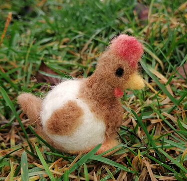 Handgefilztes braun-weißes Huhn aus Filzwolle auf Gras