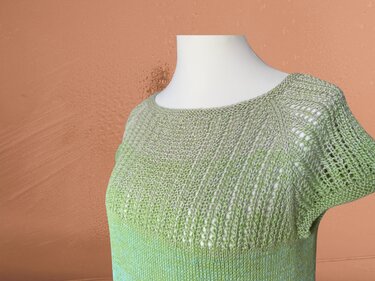 Gestricktes kurzärmeliges Damenshirt in Grüntönen mit Lochmuster auf weißer Schneiderpuppe