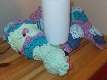 Nahaufnahme eines gehäkelten Amigurumi-Drachens mit Muschel- und Schuppenmustern in Mint, Türkis und Lila