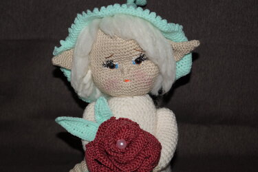 Gehäkelte Amigurumi‑Puppe mit Elfenohren hält rote Häkelrose