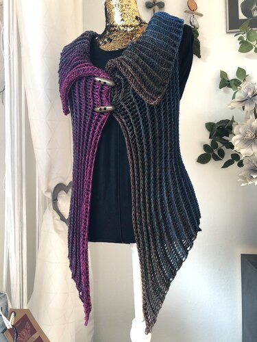 Gehäkelte Damenweste mit Farbverlauf in Magenta, Blau und Braun auf einer Schneiderpuppe, mit breitem Kragen und zwei Knebelknöpfen