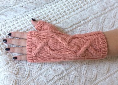 Rosa gestrickte fingerlose Armstulpe mit Zopfmuster auf hellem Strickhintergrund