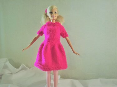 Blonde Puppe trägt ein leuchtend pinkes, kurzärmeliges Strickkleid