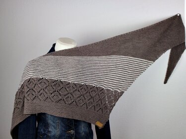 Neutral asymmetrical triangle knitted shawl with cream stripes and scalloped lace edging draped on mannequin
