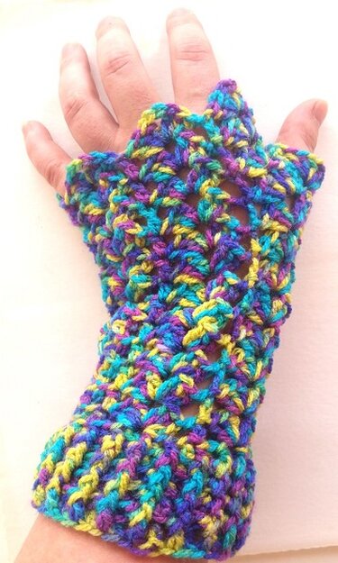 Hand mit einem bunten, gehäkelten fingerlosen Handschuh in Blau, Lila und Gelb
