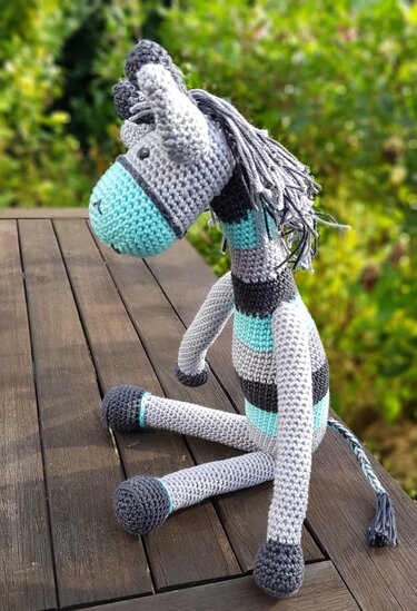 Gehäkeltes gestreiftes Zebra-Amigurumi in Grau und Türkis auf Holzbank