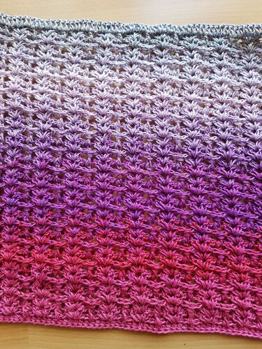 Nahaufnahme eines gehäkelten Schals in Grau, Lila und Pink mit Farbverlauf und strukturiertem Muster.