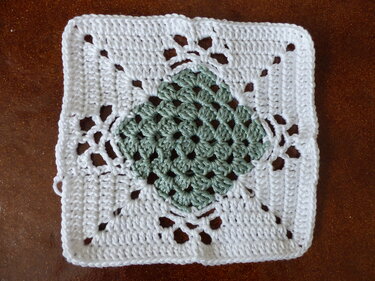 Gehäkeltes Granny Square mit grünem Zentrum und weißem Rand auf braunem Untergrund
