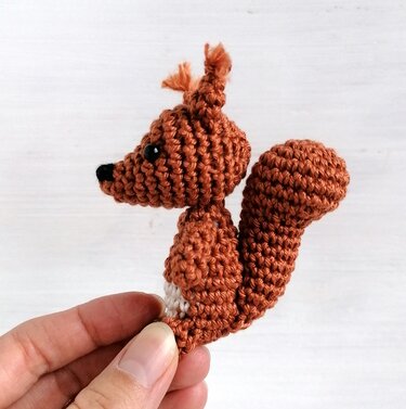 Braunes gehäkeltes Amigurumi-Eichhörnchen mit buschigem Schwanz, in einer Hand gehalten.