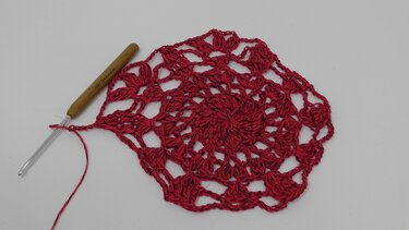 Rotes rundes Häkelmotiv mit Häkelnadel auf hellem Untergrund