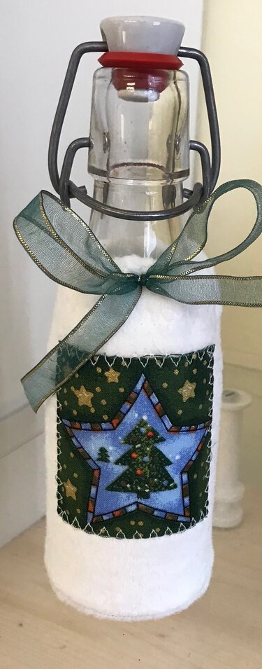 Glasflasche mit Schwingverschluss, weiße Stoffhülle und genähte Weihnachtsapplikation mit Tannenbaum, verziert mit grünem Band