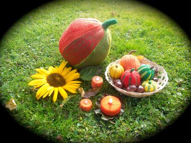 Gestrickte Herbstdekoration auf Gras mit großem Kürbis, Korb mit kleinen Kürbissen, Sonnenblume, Kastanien und gestrickten Kerzen