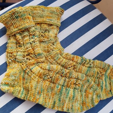 Handgestrickte Socken in Gelb-Orange-Grün mit Lochmuster auf blau-weiß gestreifter Unterlage