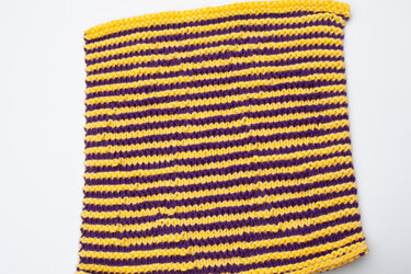 Close-up knitted swatch with alternating yellow and purple horizontal stripes.