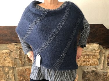 Dunkelblauer asymmetrischer Strickponcho mit diagonalen Streifen über gemusterter Bluse