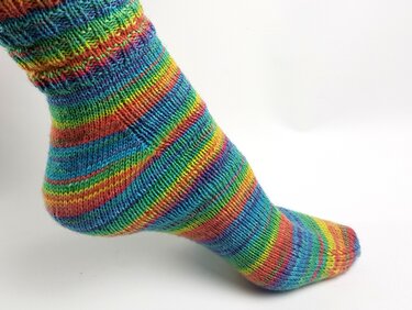 Gestrickte Socke mit Regenbogenstreifen an einem Fuß
