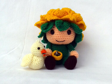 Gehäkelte Amigurumi-Puppe mit gelbem Blumenhut neben einem kleinen gehäkelten Küken