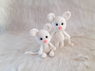 Zwei weiße gehäkelte Amigurumi‑Mäuse mit schwarzen Augen und rosa Nasen auf hellem, flauschigem Hintergrund