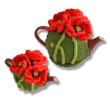 Two green handmade tea cosies with red poppy flowers on teapots against a white background.
