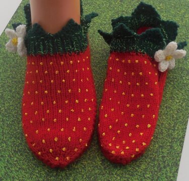 Paar rote gestrickte Kindersocken im Erdbeer-Look mit grünem gezacktem Bündchen und weißen Blumen
