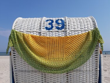 Gehäkeltes Halbrundtuch in Gelb‑Grün auf weißem Strandkorb