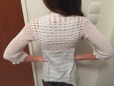 Rückenansicht einer Person mit einem weißen, gehäkelten Bolero mit Lochmuster und Drei-viertel-Ärmeln.