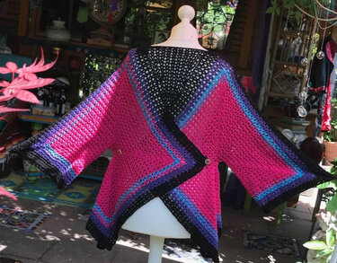 Gehäkelte Damenjacke auf einer Schaufensterpuppe in Pink, Schwarz und Blau mit weiten Ärmeln.