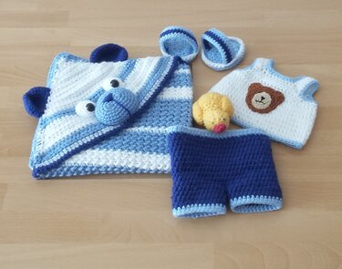 Gehäkeltes blau-weißes Babyset: Decke mit Bärenkapuze, Oberteil mit Bärenapplikation, Shorts, Schühchen und kleine gelbe Amigurumi-Ente.