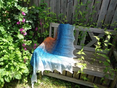 Gestricktes Dreieckstuch in Blau und Orange mit Lochmuster auf Holzbank im Garten