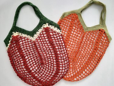 Zwei gehäkelte Netztaschen in Rot und Orange mit grünen Henkeln auf hellem Hintergrund
