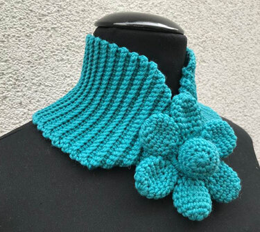 Türkisfarbener gehäkelter Kragenschal mit geripptem Kragen und großer Blüte an einer schwarzen Schaufensterpuppe.