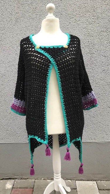 Gehäkelter schwarzer Cardigan mit türkiser Kante, violetten Ärmelabschlüssen und Quasten auf einer Schneiderpuppe