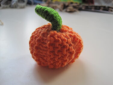 Gestrickter orangefarbener Zierkürbis mit grünem Stiel auf hellem Untergrund