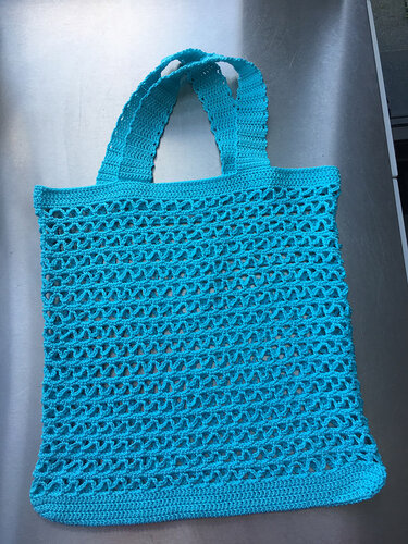 Türkise gehäkelte Netztasche mit breiten Henkeln auf metallischer Fläche
