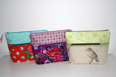 Drei Stofftaschen mit Reißverschluss in unterschiedlichen Mustern und Farben auf weißem Untergrund, darunter Blumen-, Punkte- und Vogelmotiv.