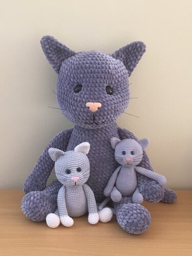 Große lilafarbene gehäkelte Katze aus samtigem Garn mit zwei kleineren grauen Amigurumi-Kätzchen, eines mit weißen Pfoten und Ohren