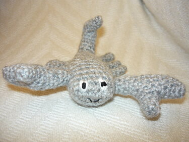 Nahaufnahme eines grau gehäkelten Flusskrebs-Amigurumis mit gestickten Augen auf hellem Stoff