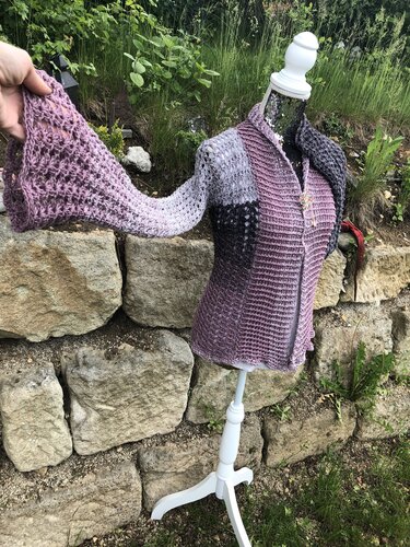 Gehäkelte offene Damenjacke in Grau und Lila auf Schaufensterpuppe vor Natursteinmauer