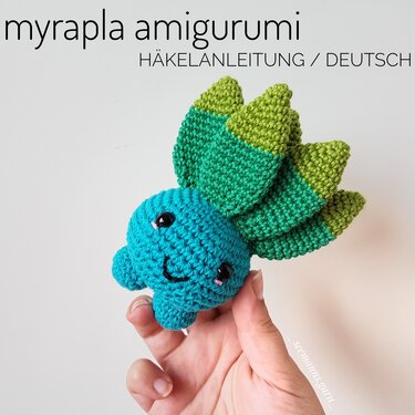 Hand hält handgroßes türkisgrünes Amigurumi mit lächelndem Gesicht und gestuften grünen Blättern