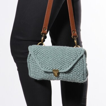 Light blue knitted shoulder bag with textured stitch, flap closure and brass turn lock, worn with black leggings.