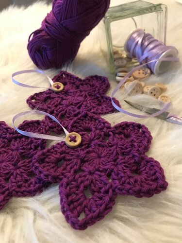 Nahaufnahme von schnell gehäkelten violetten Blumenapplikationen mit Holzknöpfen, Garn und Satinband