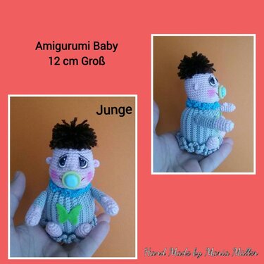 Handgehaltenes gehäkeltes Amigurumi-Babyjunge (ca. 12 cm) mit dunkelbraunem Haar, blauem Schnuller und grüner Schmetterlingsapplikation am Strampler.