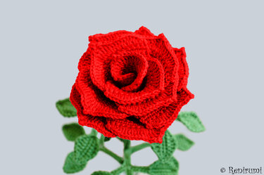 Kräftig rote gehäkelte Rose mit grünen Blättern