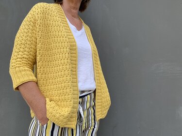 Senfgelbe Strickjacke mit Strukturmuster, gerippter Einfassung und aufgesetzten Taschen über weißem T‑Shirt
