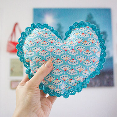 Herzförmiges hellblaues Kissen mit Blumenmuster und blauer Spitze in einer Hand