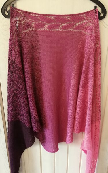 Gestricktes Tuch in Pink- und Violetttönen mit Farbverlauf und zartem Lochmuster am oberen Saum, an einem Kleiderbügel hängend.